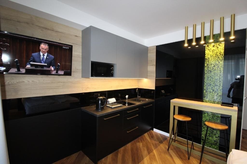 A modern kitchen with a built-in microwave, a coffee machine, and a wooden countertop. There is a bar area with stools and a television mounted on the wall.