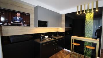 A modern kitchen with a built-in microwave, a coffee machine, and a wooden countertop. There is a bar area with stools and a television mounted on the wall.