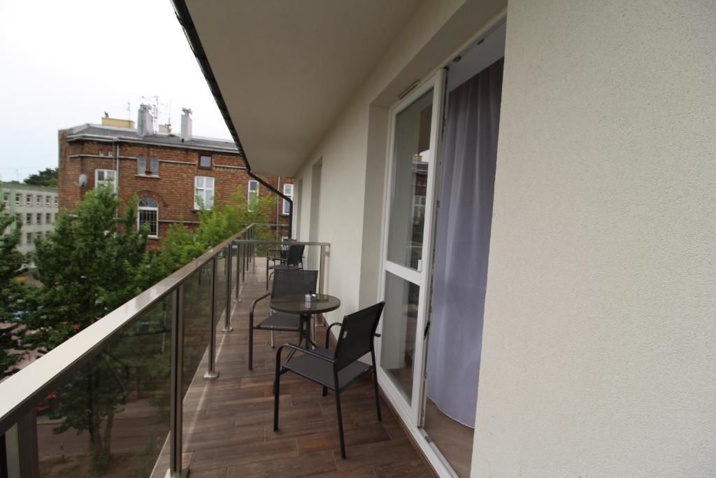 Un balcon avec une table et des chaises, une balustrade en verre et une vue sur un immeuble en briques.