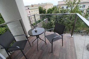 A balcony with two chairs and a small table, overlooking a street with buildings and trees. - Apartamenty Nowa Kamienica (Czestochowa)
