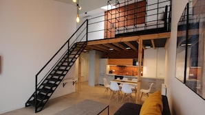 A modern loft apartment with a staircase leading to a mezzanine, a kitchen area, and a dining space. - Apartamenty Nowa Kamienica (Czestochowa)