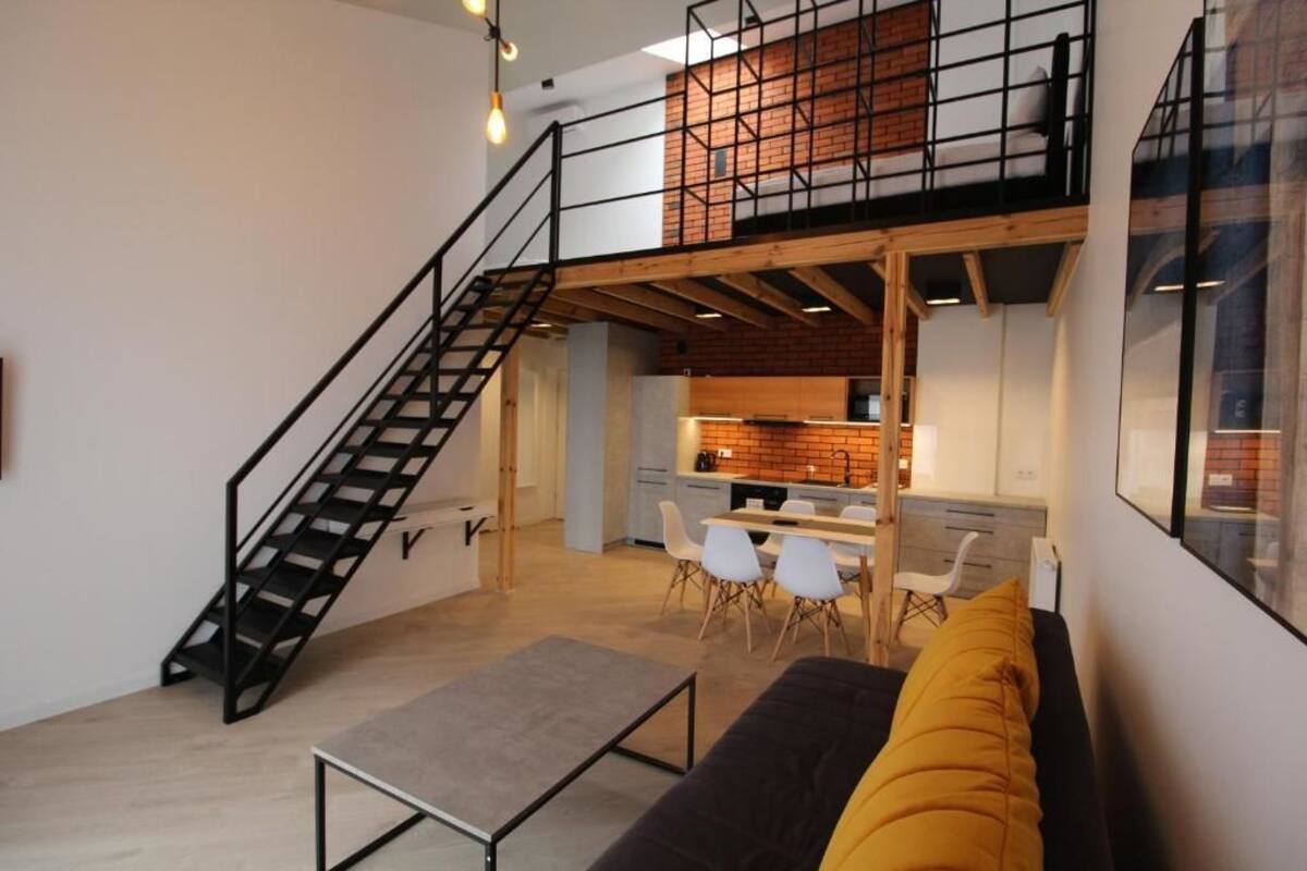 A modern loft apartment with a staircase leading to a mezzanine, a kitchen area, and a dining space.