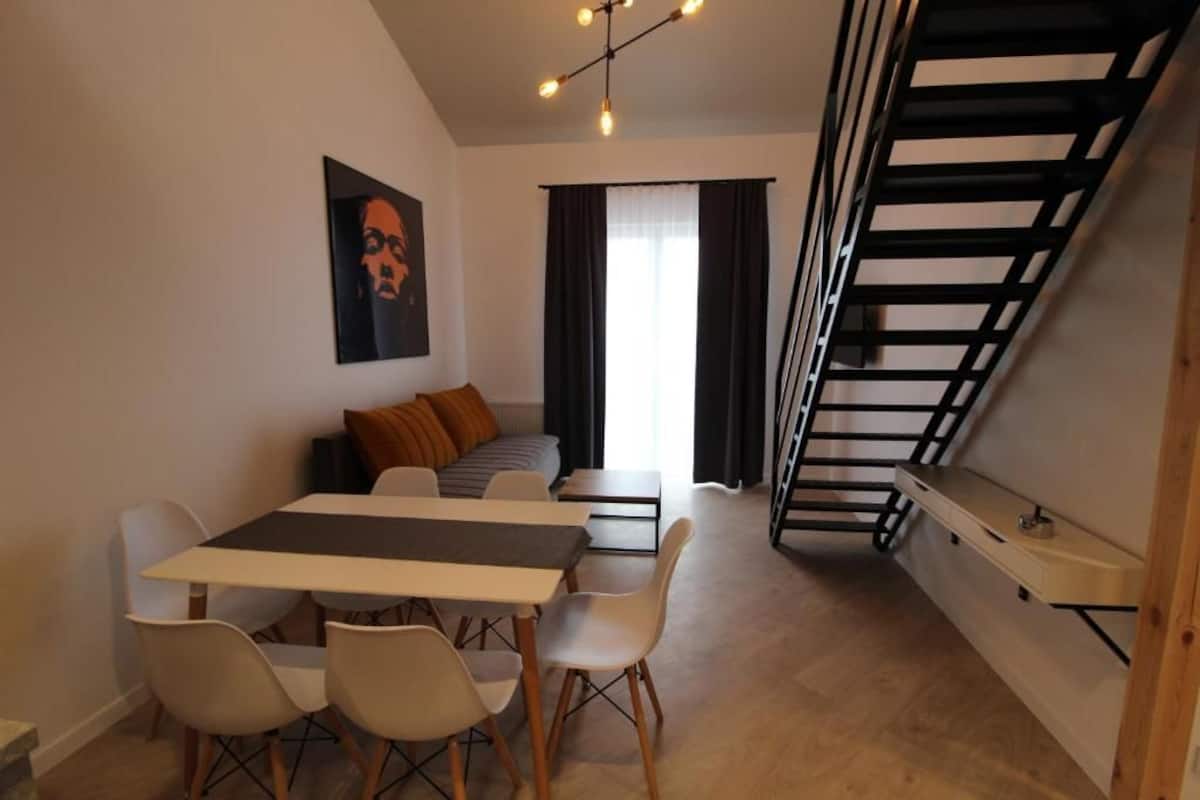 A modern living space with a dining area, a sofa, and a staircase.