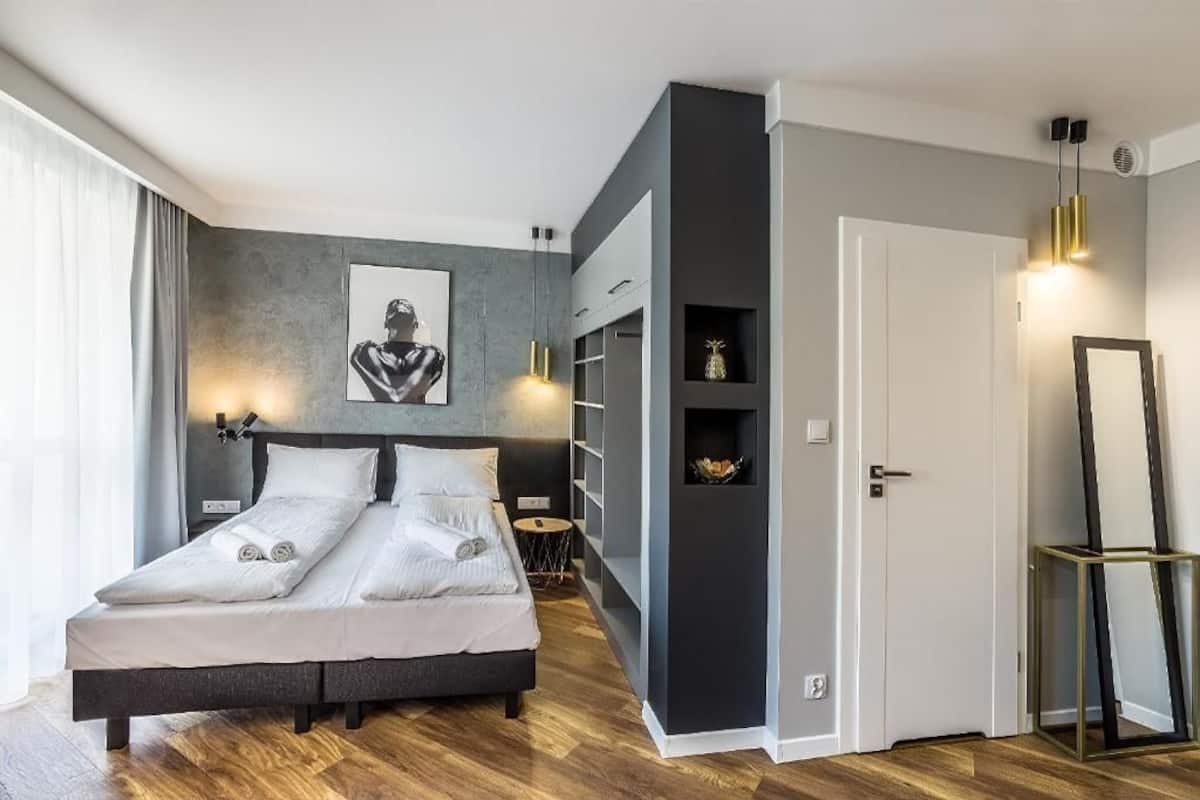A modern bedroom with a bed, bedside tables, a wardrobe, and a large mirror.