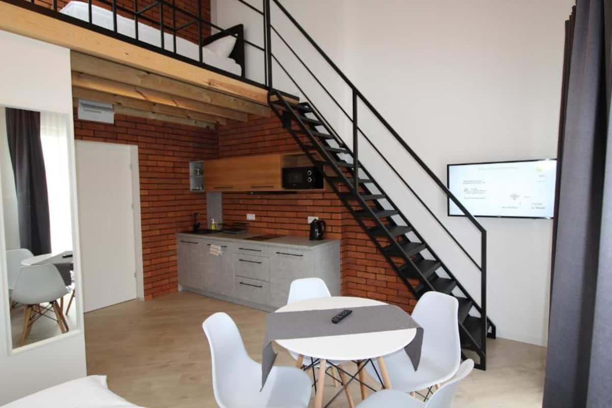 A modern kitchen with a brick wall, a staircase, and a dining area with white chairs and a table.