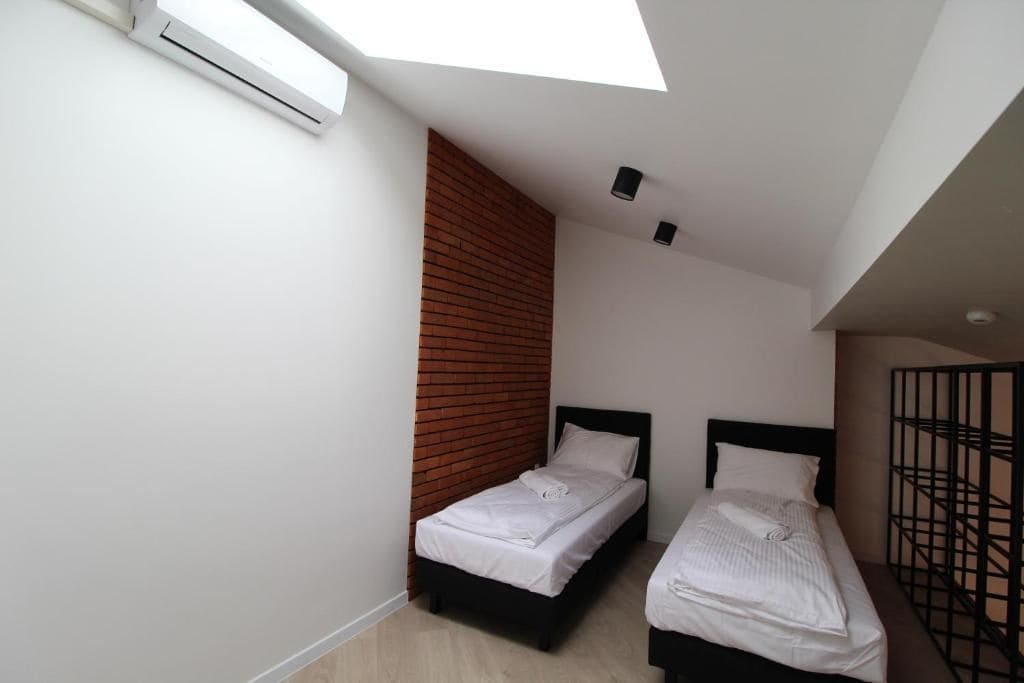 A small, modern room with two beds, a skylight, and a brick accent wall.