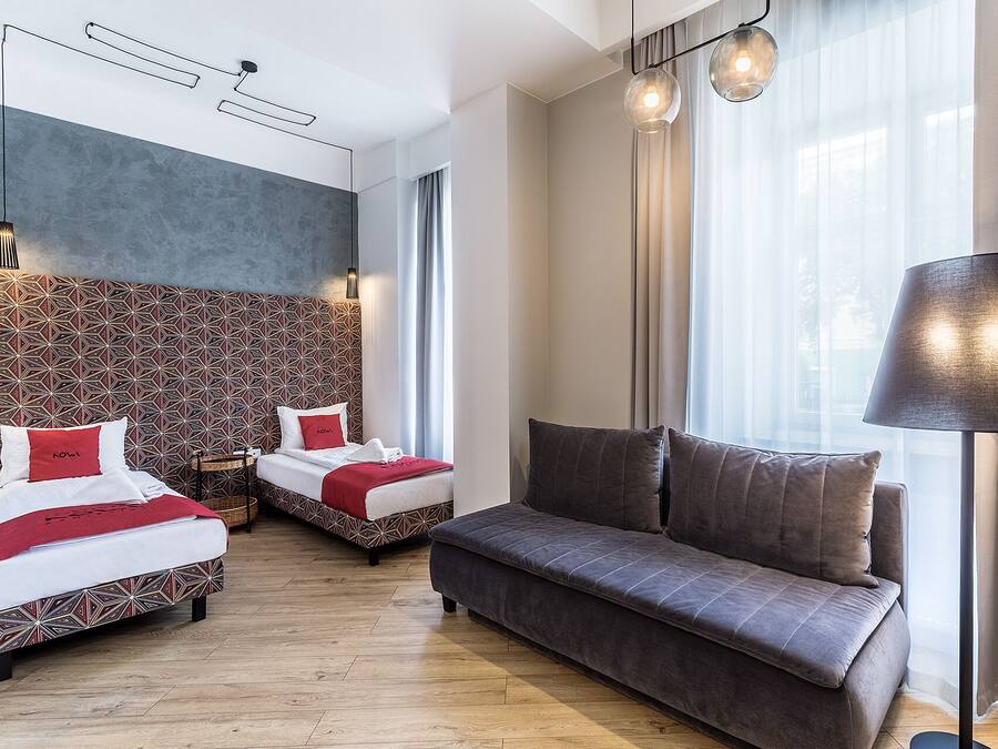 A hotel room with two beds, a sofa, and a large window with curtains.