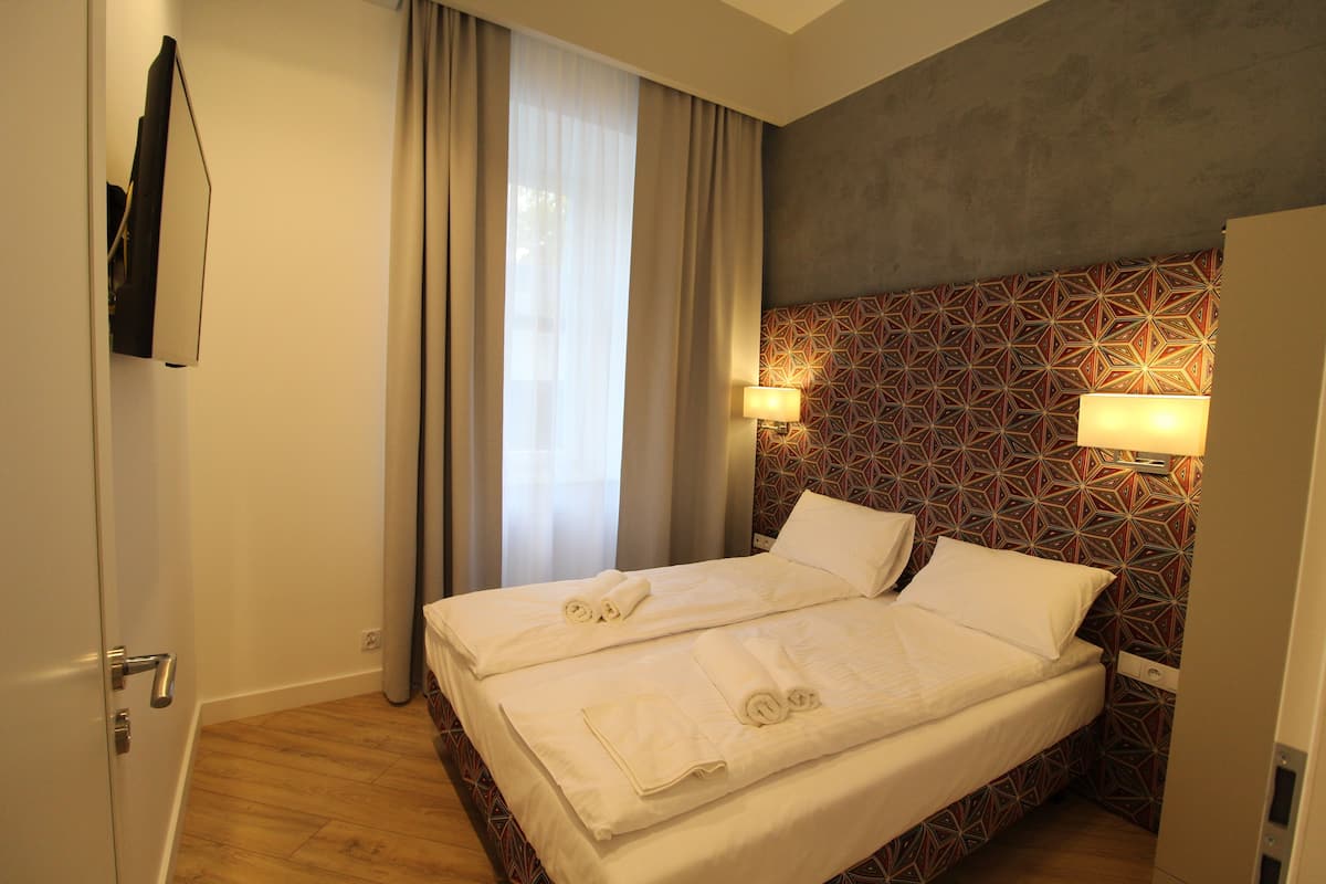 A hotel room with a bed, two bedside lamps, a patterned wall, and a window with curtains.