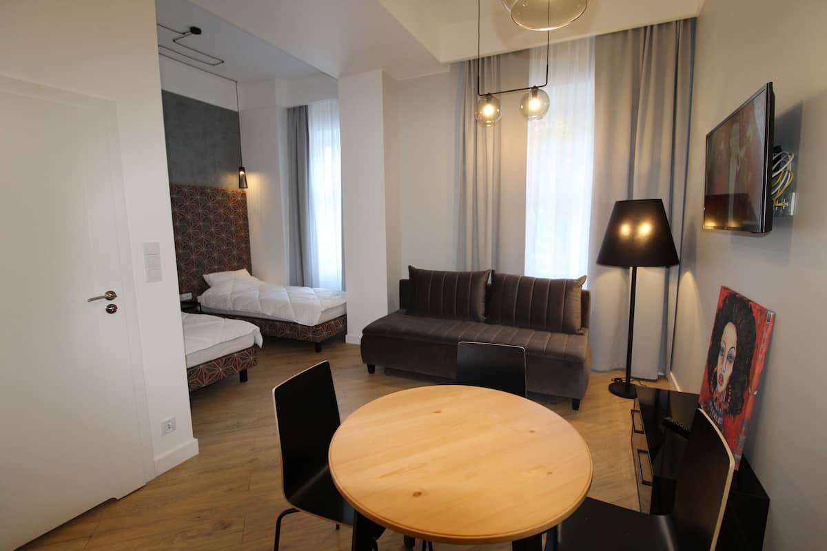 A compact hotel room with a bed, a sofa, a dining table, and a TV mounted on the wall.