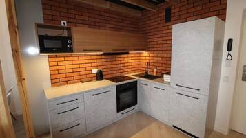A compact kitchen with a brick backsplash, a microwave, a stove, and a refrigerator.