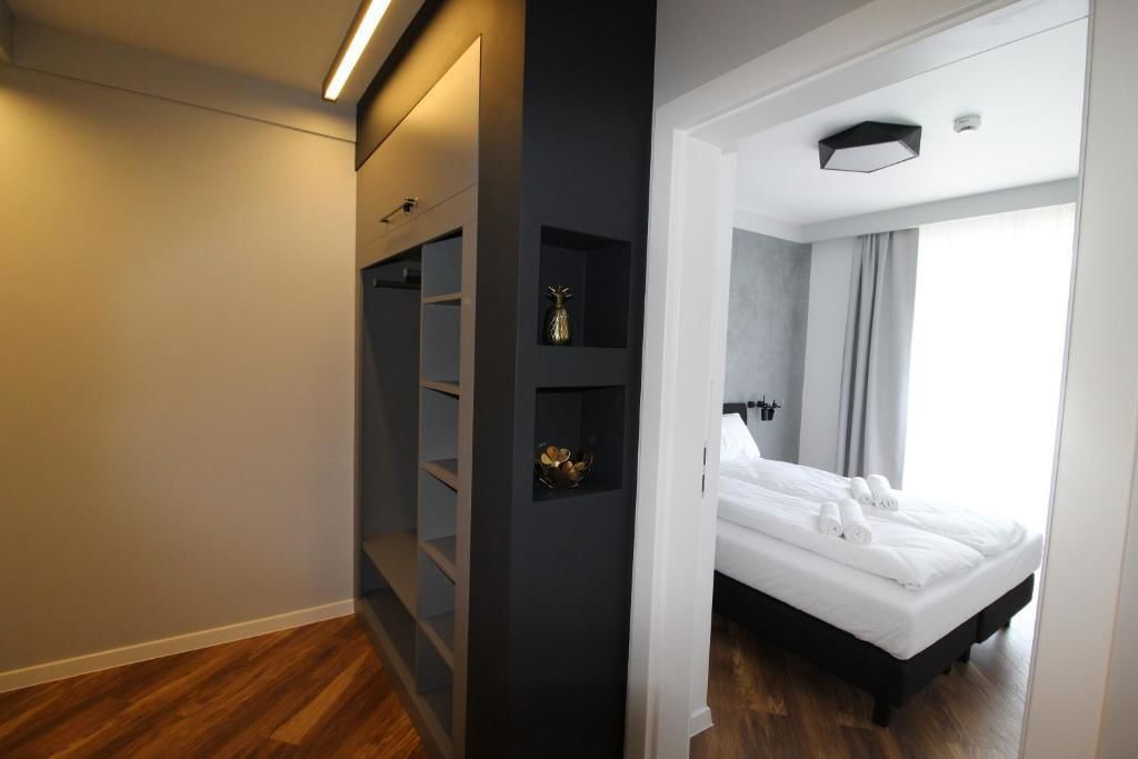 A modern hotel room with a bed, a wardrobe, and a small shelf with decorative items.