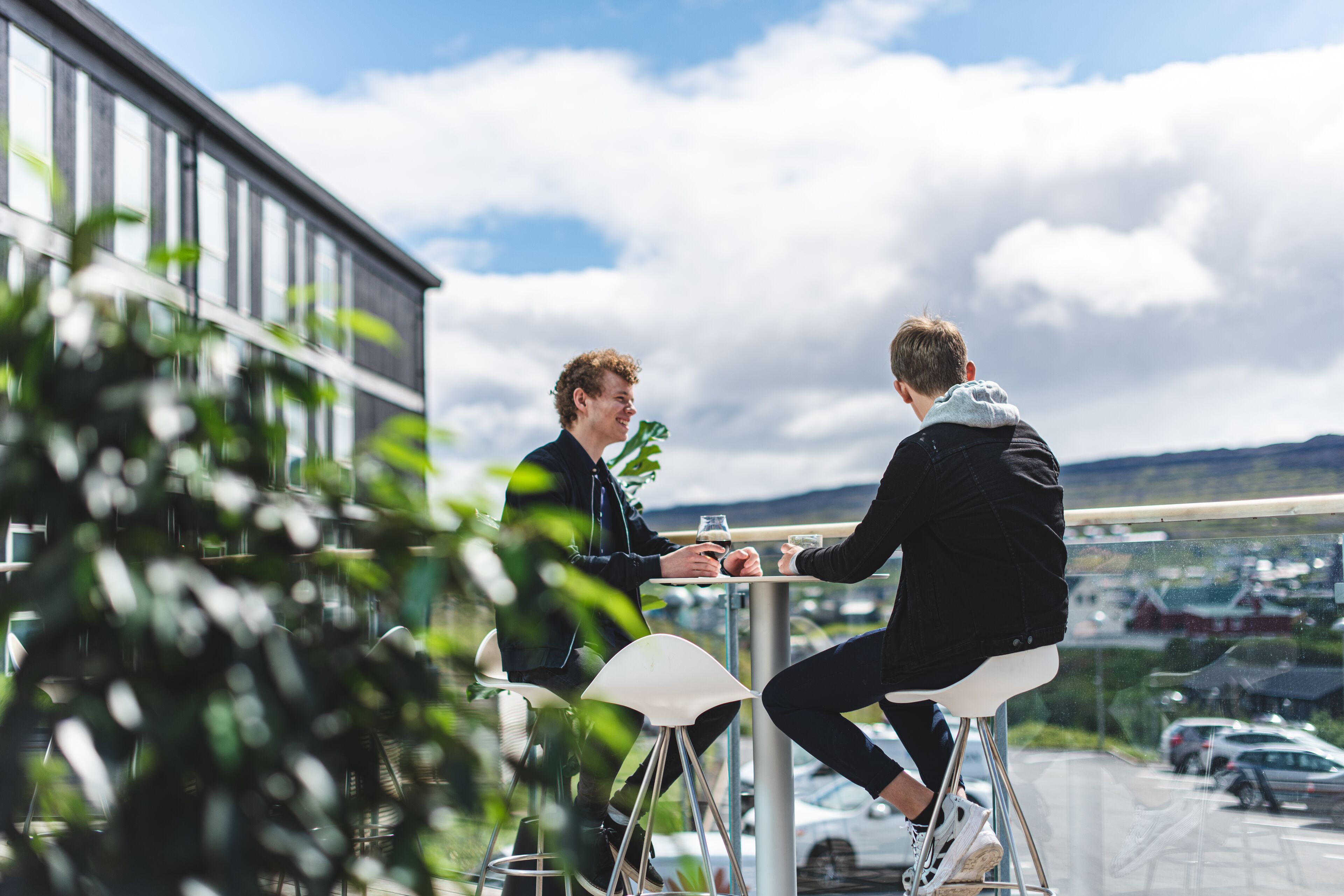Two people sitting at a table outdoors with a view of a parking lot and buildings in the background.