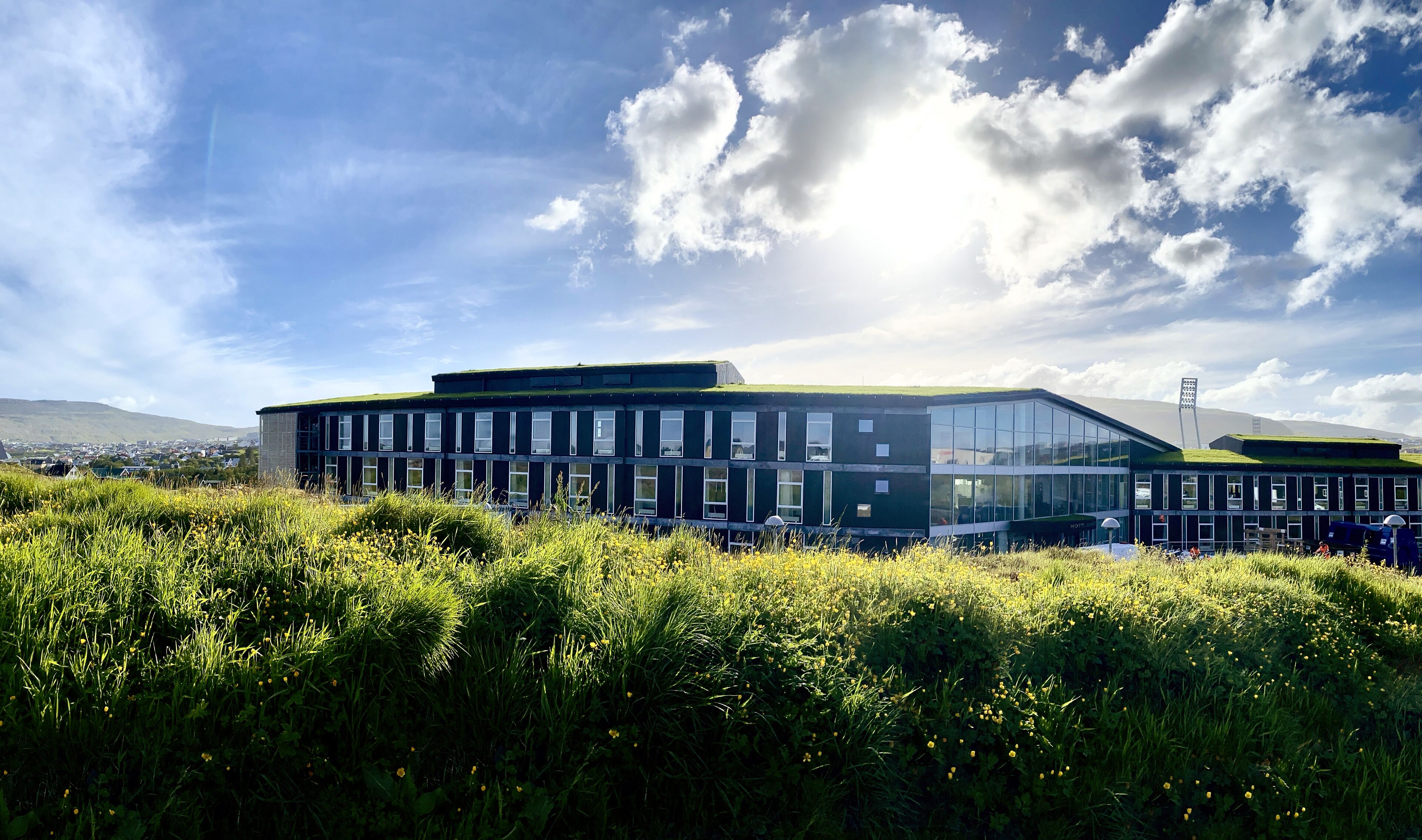 A modern building with a glass facade, surrounded by lush greenery and a clear sky.