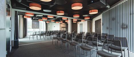 A conference room with rows of chairs, ceiling lights, and large windows.