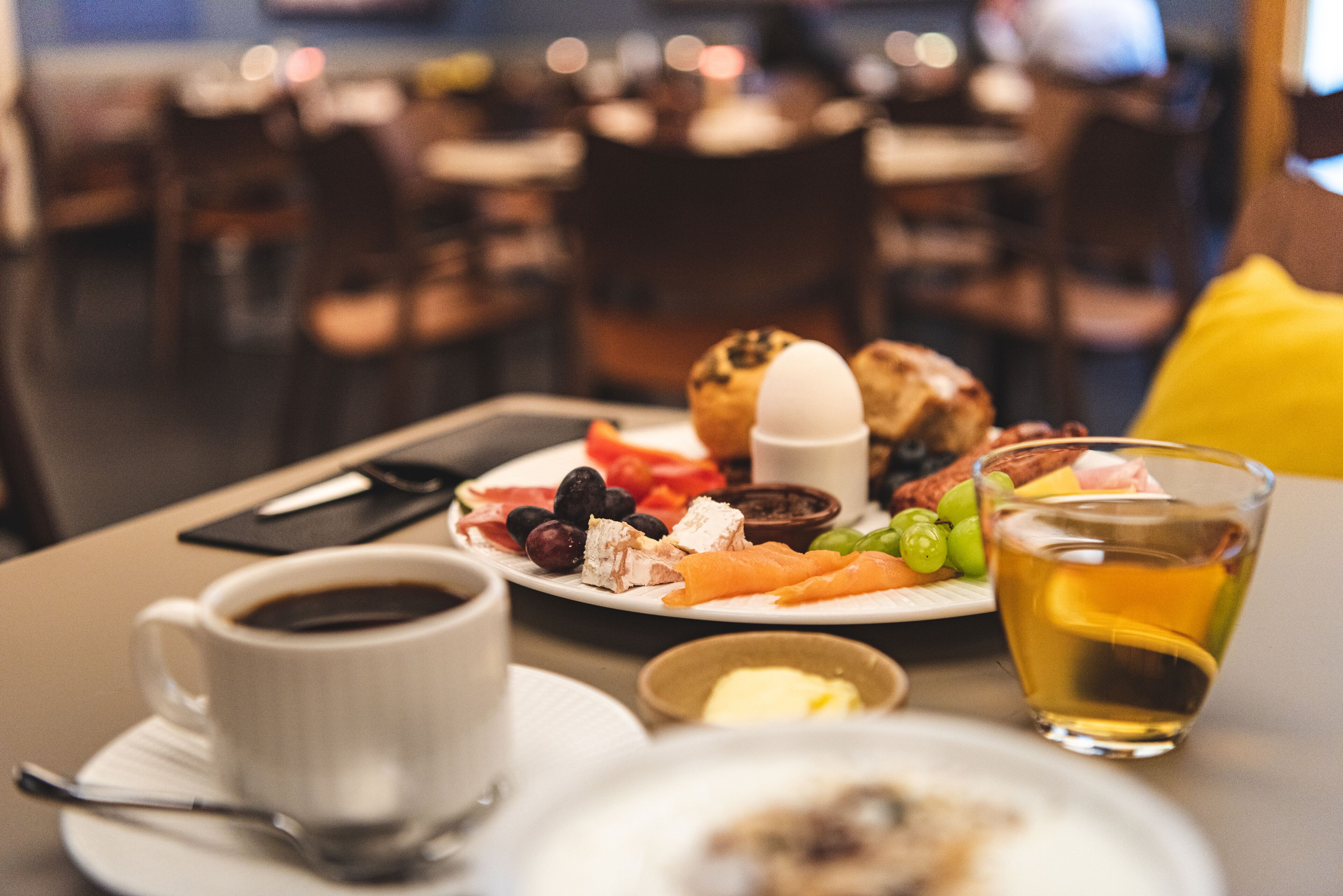 Een ontbijttafel met een kop koffie, een glas thee, een bord met eieren, toast en fruit.