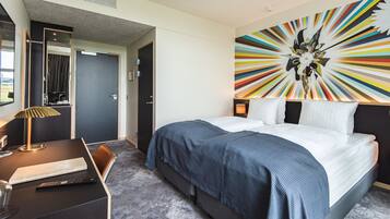 A hotel room with a bed, a desk, and a mirror.
