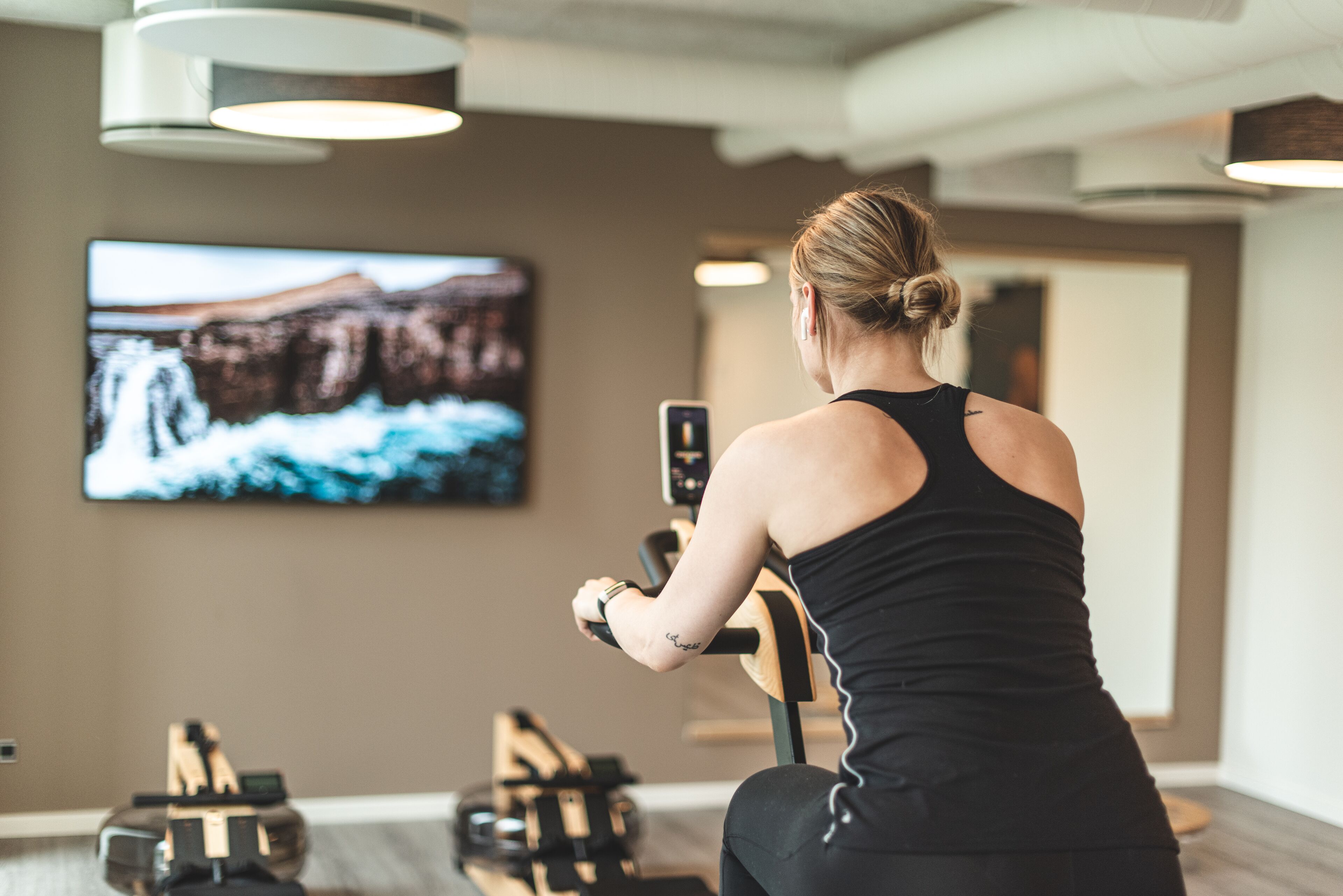 A person using a stationary bike in a gym with a large TV screen displaying a nature scene.