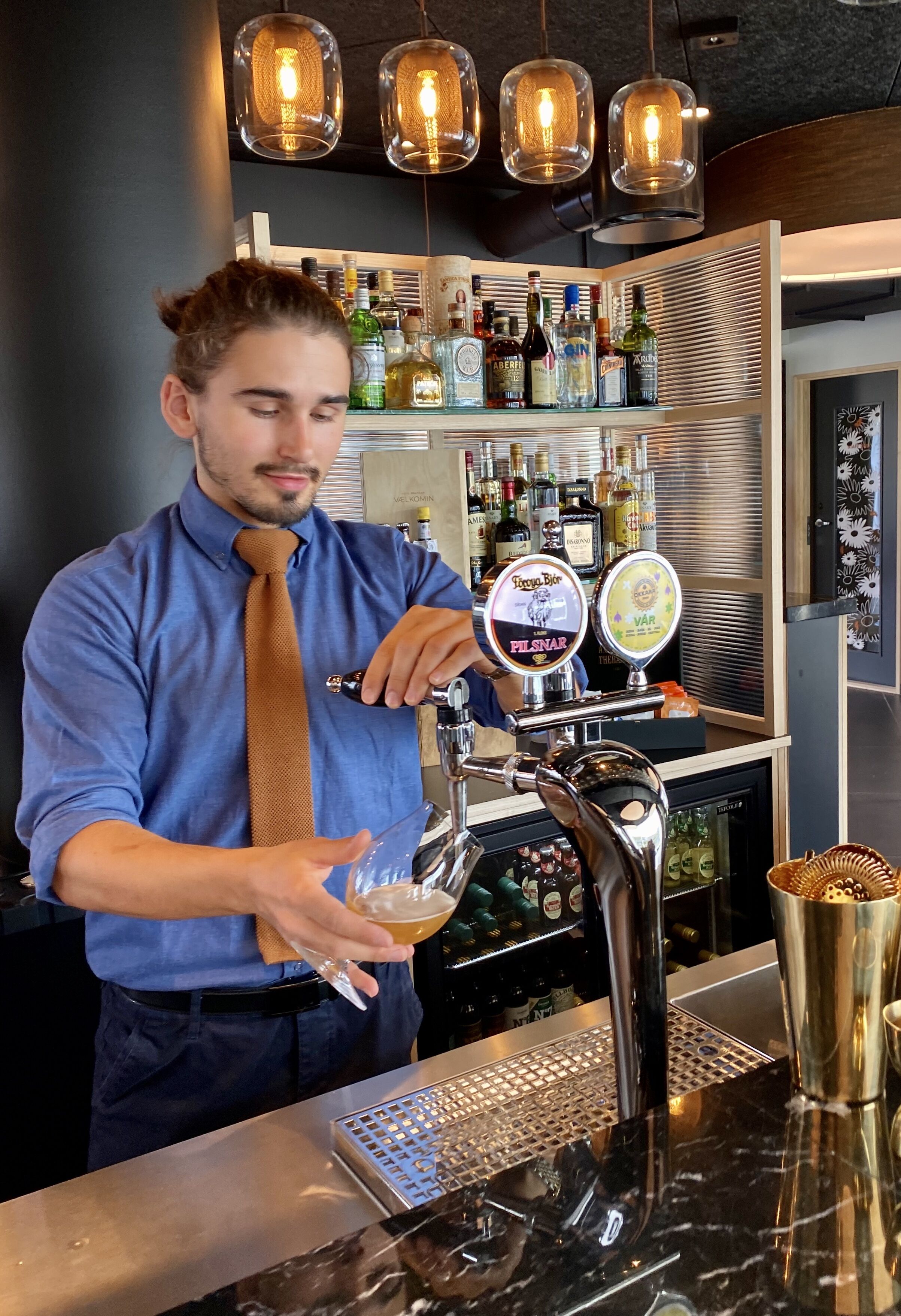 A bartender pouring a drink from a tap labeled "Pilsner" into a glass.