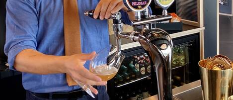 A bartender pouring a drink from a tap labeled "Pilsner" into a glass.