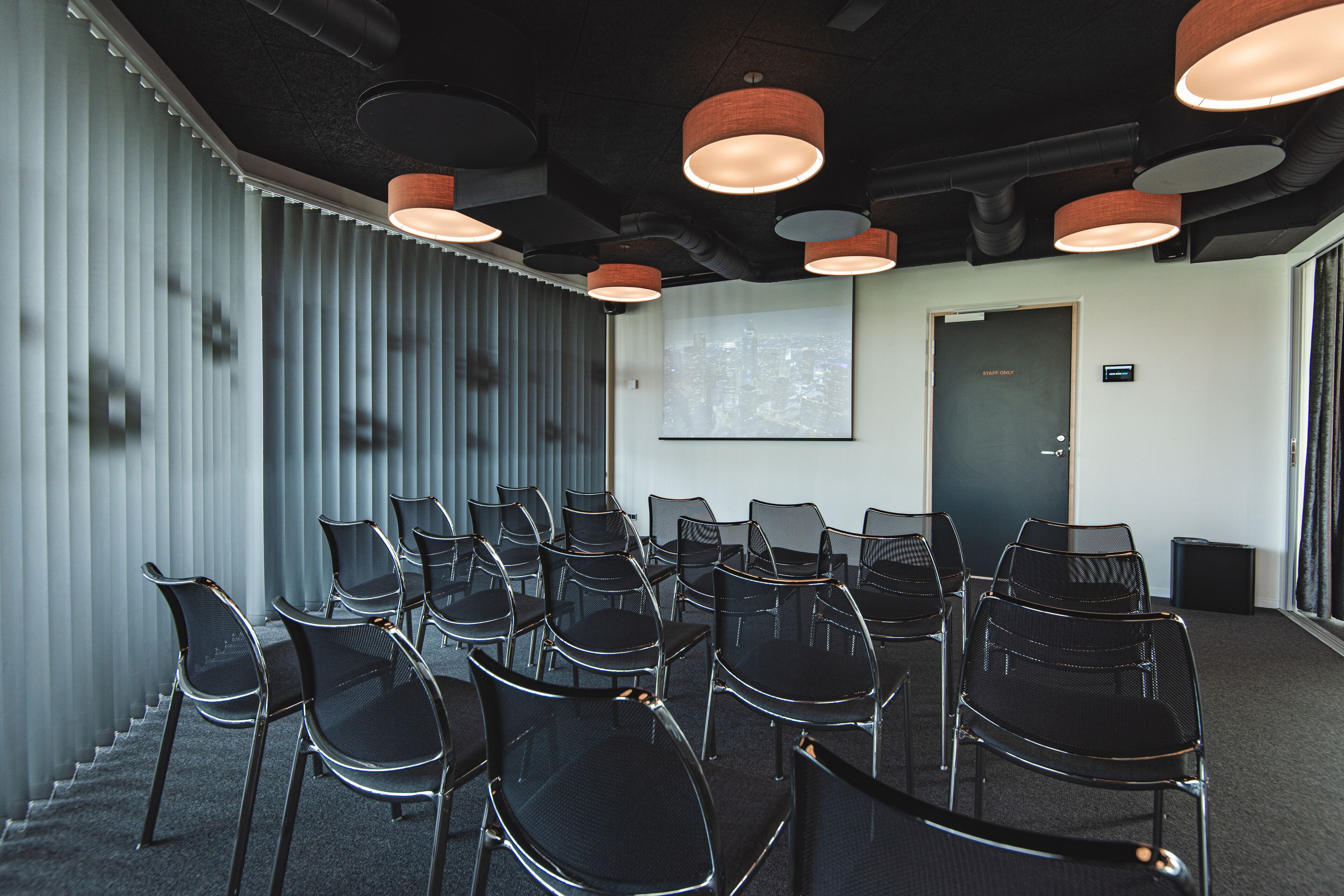A conference room with black chairs arranged around a table, a projector screen on the wall, and a door labeled "Staff Only".