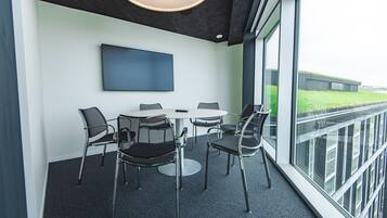 Una sala de reuniones moderna con una mesa redonda, cuatro sillas, un televisor de pantalla plana y grandes ventanales que ofrecen vistas al exterior.