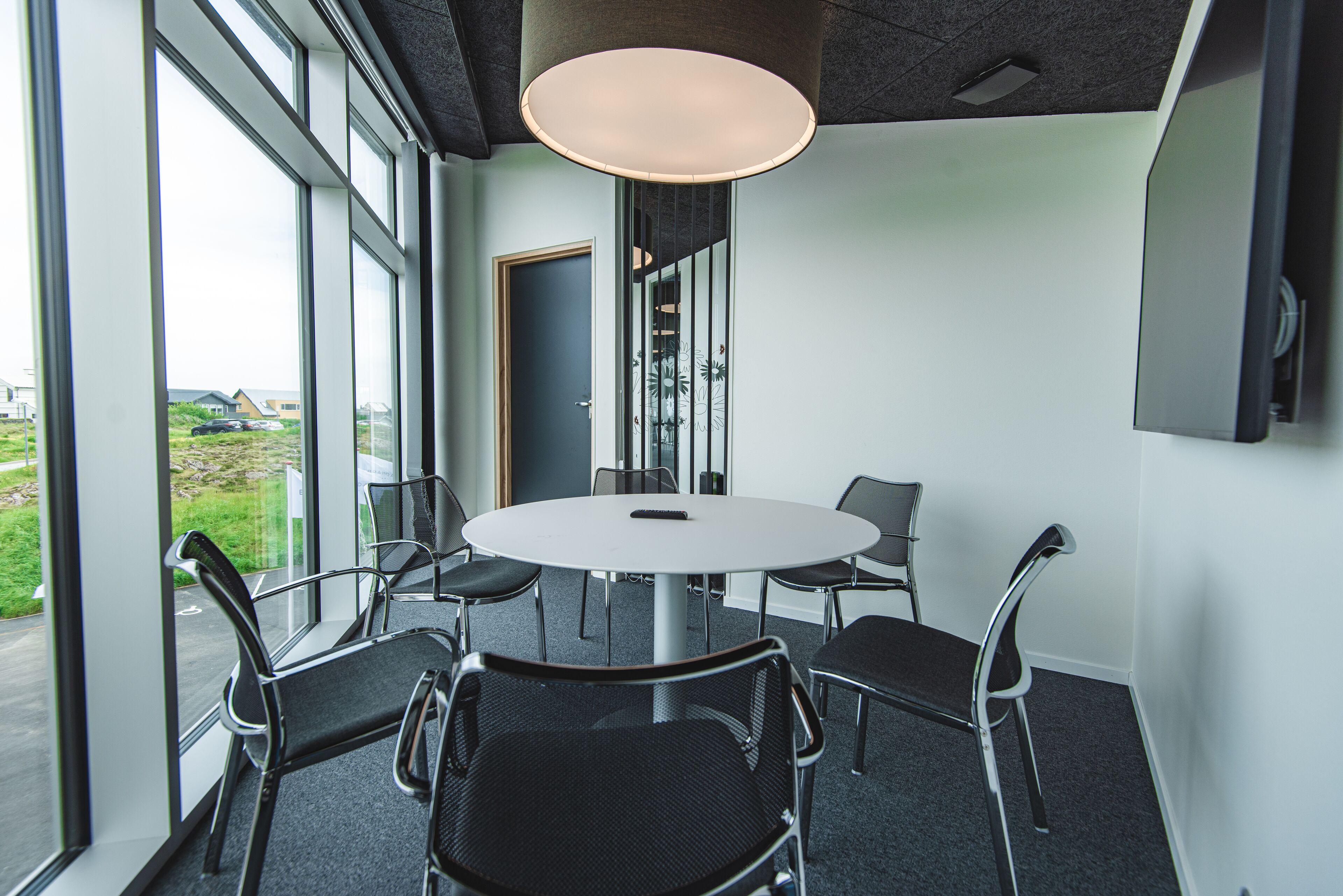 A conference room with a round table, six chairs, and large windows offering a view of the outdoors.
