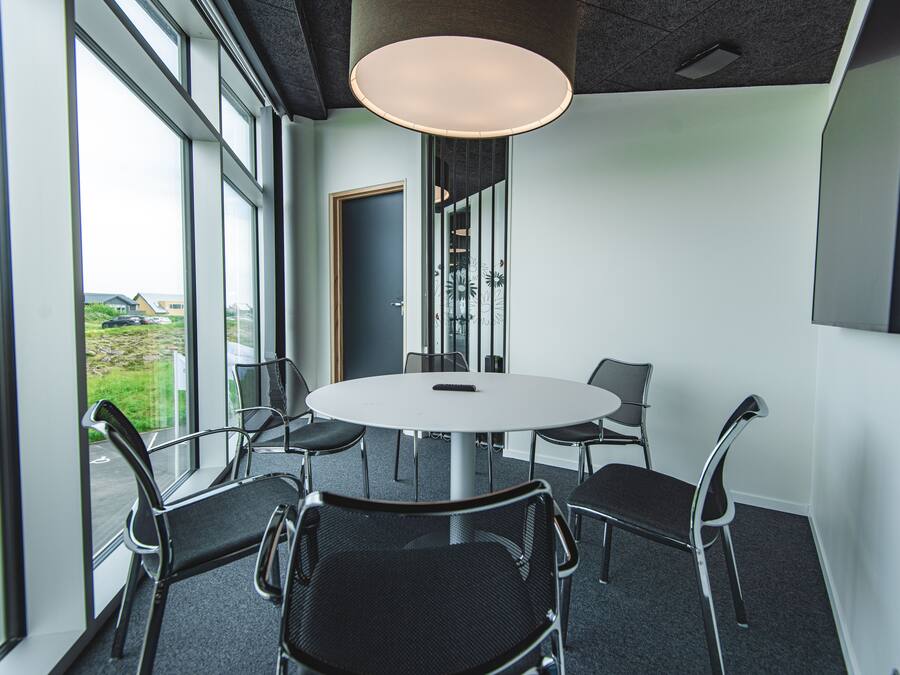 Une salle de conférence équipée d’une table ronde, de six chaises et de grandes fenêtres donnant sur l’extérieur.