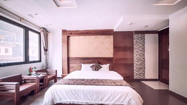A modern hotel room with a large bed, wooden furniture, a view of the city, and a small table with decorative items. - Greenland Sa Pa Hotel by DLMH (Sa Pa)