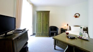 A hotel room with a television, a cabinet, a desk with a glass of wine, a bottle of water, and a small table. - Obere Mühle (Bad Elster)