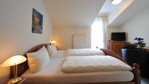A hotel room with two beds, a TV, a desk, and a painting on the wall. - Obere Mühle (Bad Elster)