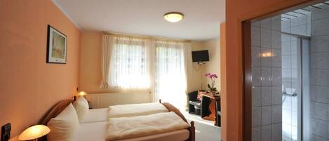 A hotel room with a bed, bedside lamp, a television on the wall, and a window with curtains.
