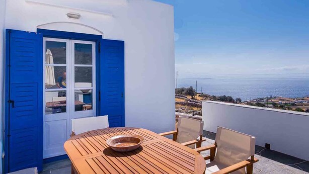 A balcony with a wooden table and chairs, a blue door, and a view of the sea. - Spacious 2 Bedroom House with Fantastic Yard (Sifnos)