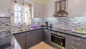 A modern kitchen with dark wood cabinets, a black countertop, and a tiled backsplash. - Spacious 2 Bedroom House with Fantastic Yard (Sifnos)