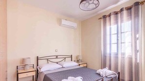 A neatly arranged bedroom with a bed, bedside tables, an air conditioning unit, and a window with curtains. - Spacious 2 Bedroom House with Fantastic Yard (Sifnos)