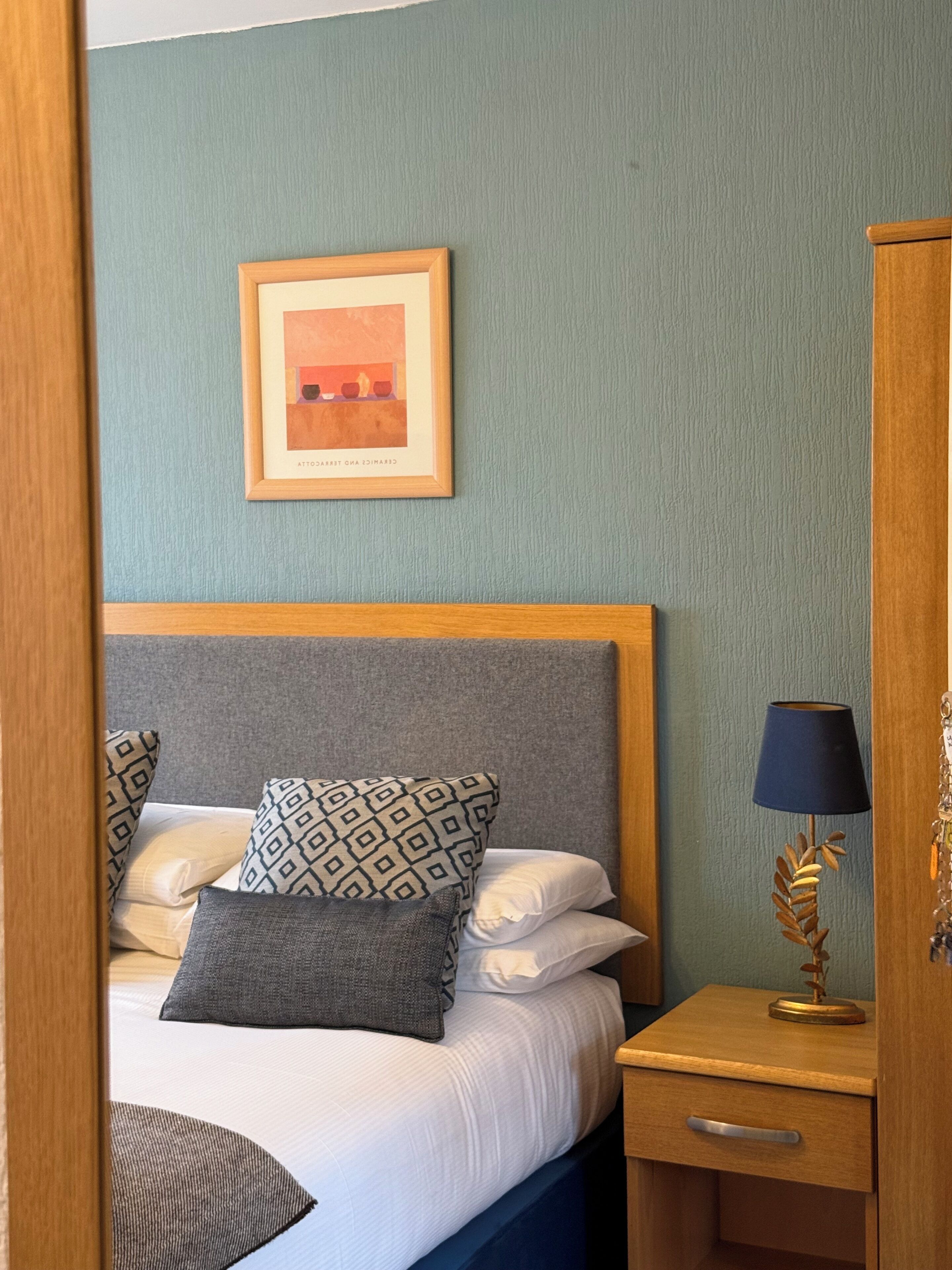 Een net opgemaakt bed met gestreepte kussens, een bedlampje en een ingelijst beeld aan de muur.