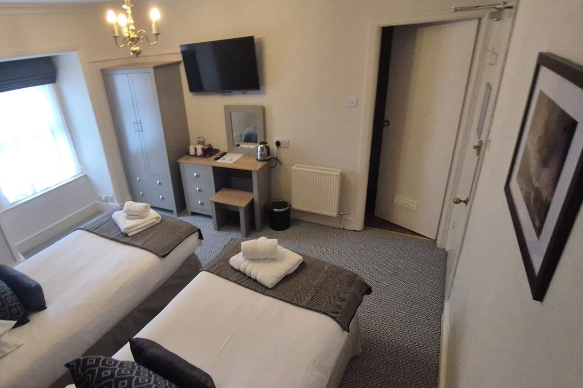 A hotel room with two beds, a desk, a television, and a window.