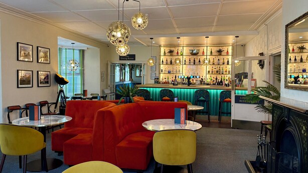 Eine Bar mit verschiedenen Flaschen, ein Kamin und ein Essbereich mit roten Sofas und gelben Stühlen.