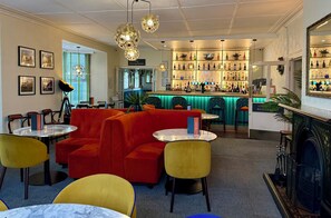 Een bar met verschillende flessen, een open haard en een eetgedeelte met rode banken en gele stoelen.