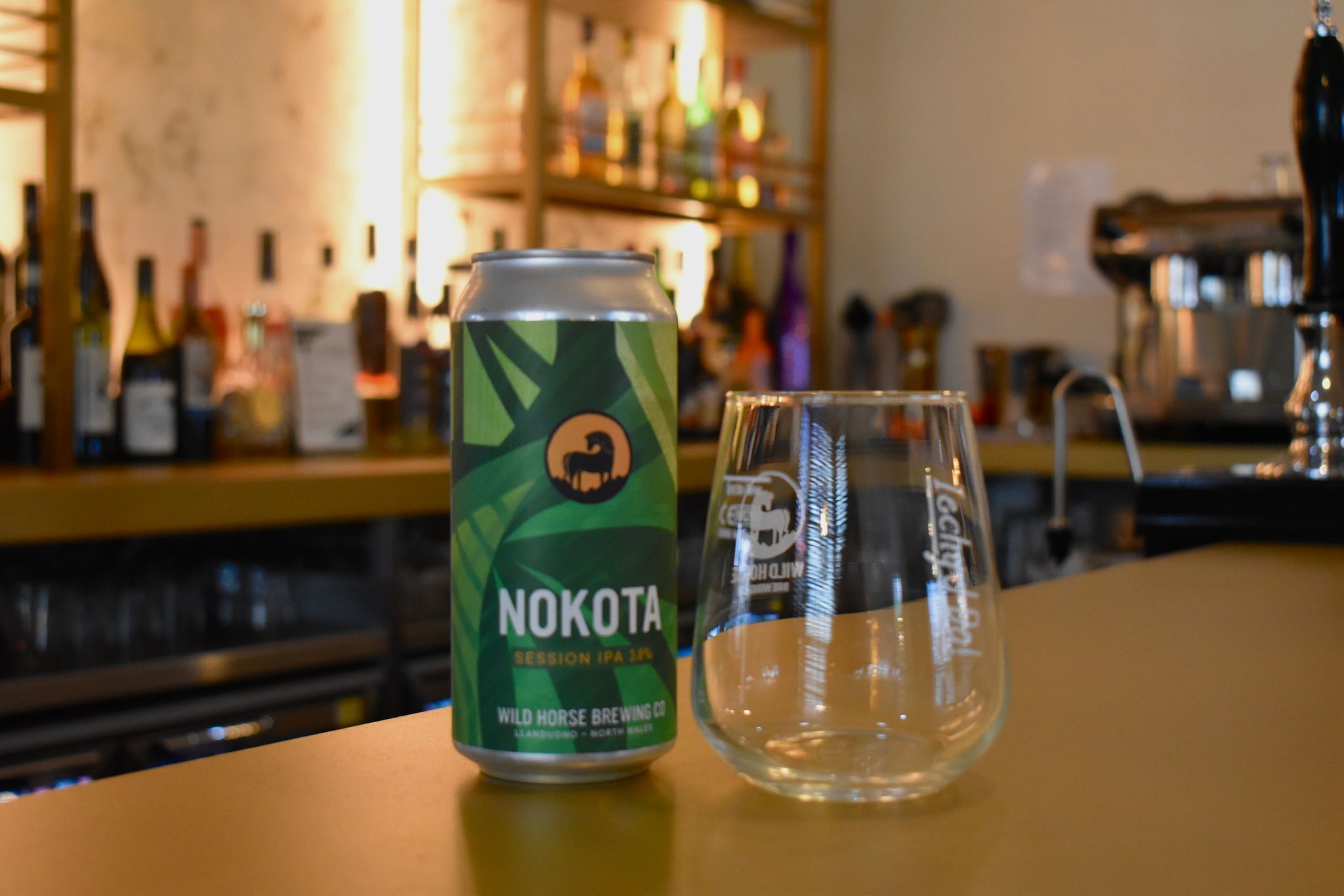 A can of beer and an empty glass on a bar counter.