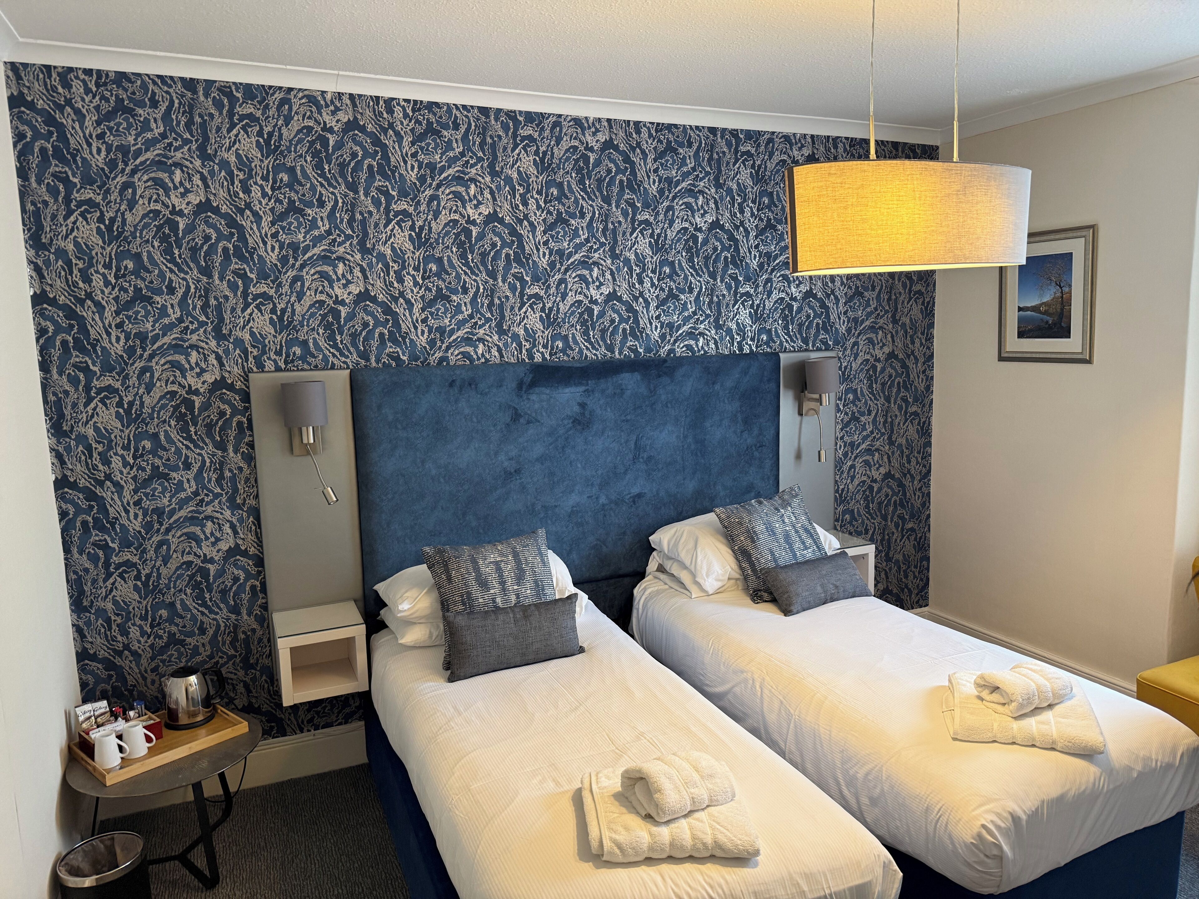 Une chambre d’hôtel avec deux lits, une table de chevet, une lampe et un mur orné d’un motif bleu.