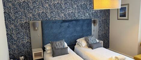 Une chambre d’hôtel avec deux lits, une table de chevet, une lampe et un mur orné d’un motif bleu.