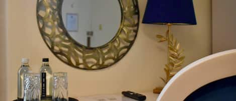 A hotel room with a round mirror, a blue lamp, and a tray with three glasses and two bottles.