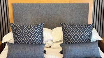 Una cama con cabecera gris, dos almohadas estampadas y una almohada blanca.