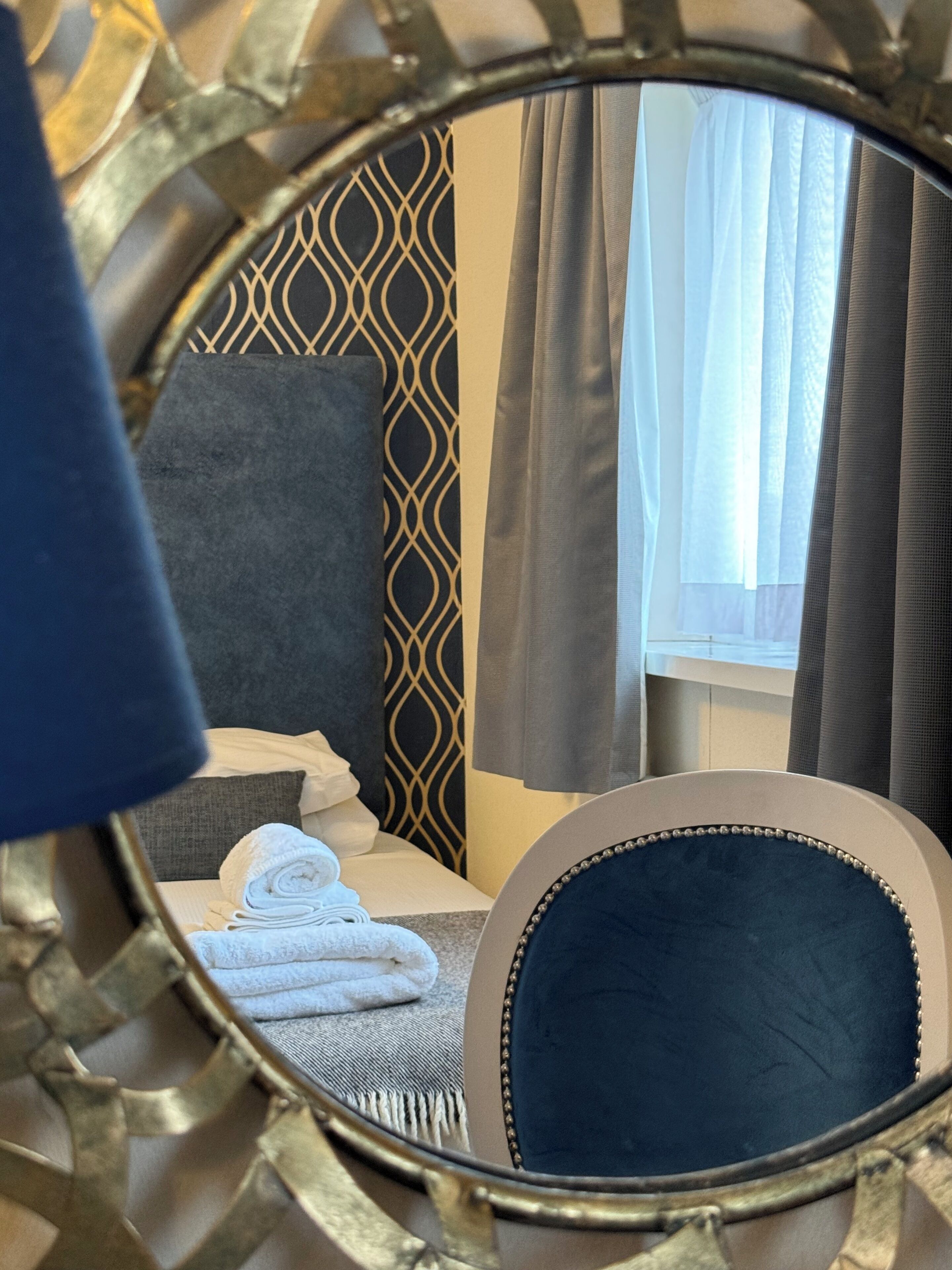 A bed with a patterned headboard, a mirror, and a window with curtains.