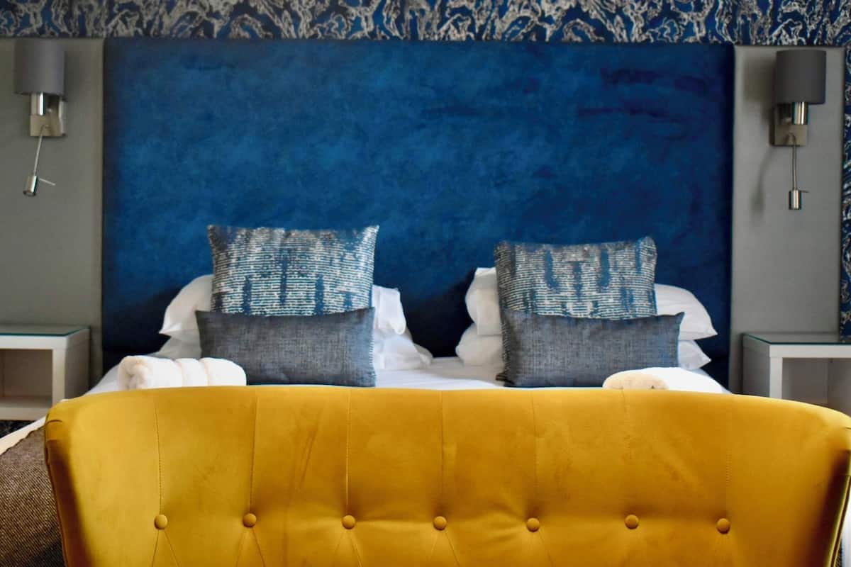 A bed with a yellow headboard, two pillows, and a blue textured wall behind.