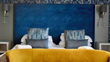 A bed with a yellow headboard, two pillows, and a blue textured wall behind.