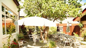Eine Terrassengruppe mit Tischen und Stühlen, umgeben von Blumentöpfen und einem Baum.