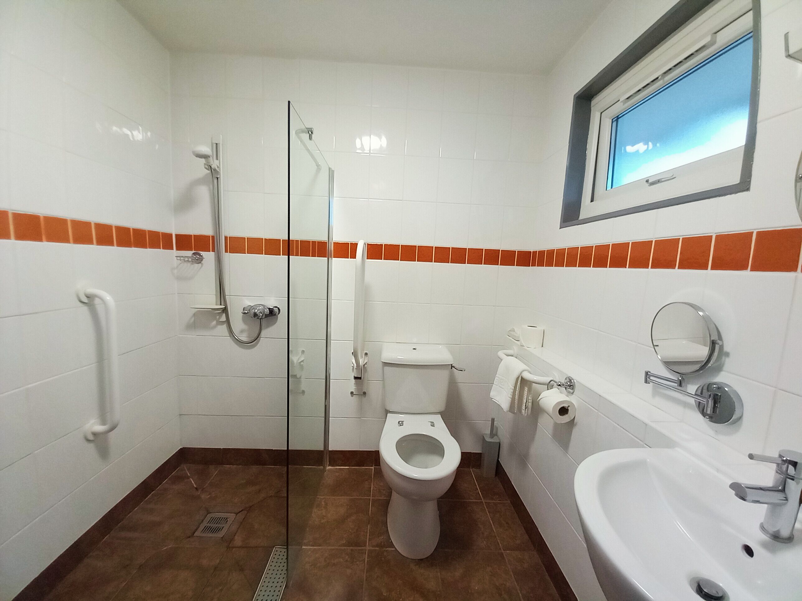 A bathroom with a glass shower enclosure, a toilet, a sink, and a window.