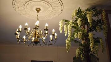 A chandelier with multiple candle-like lights, a decorative ceiling medallion, and a large artificial white flowering plant.