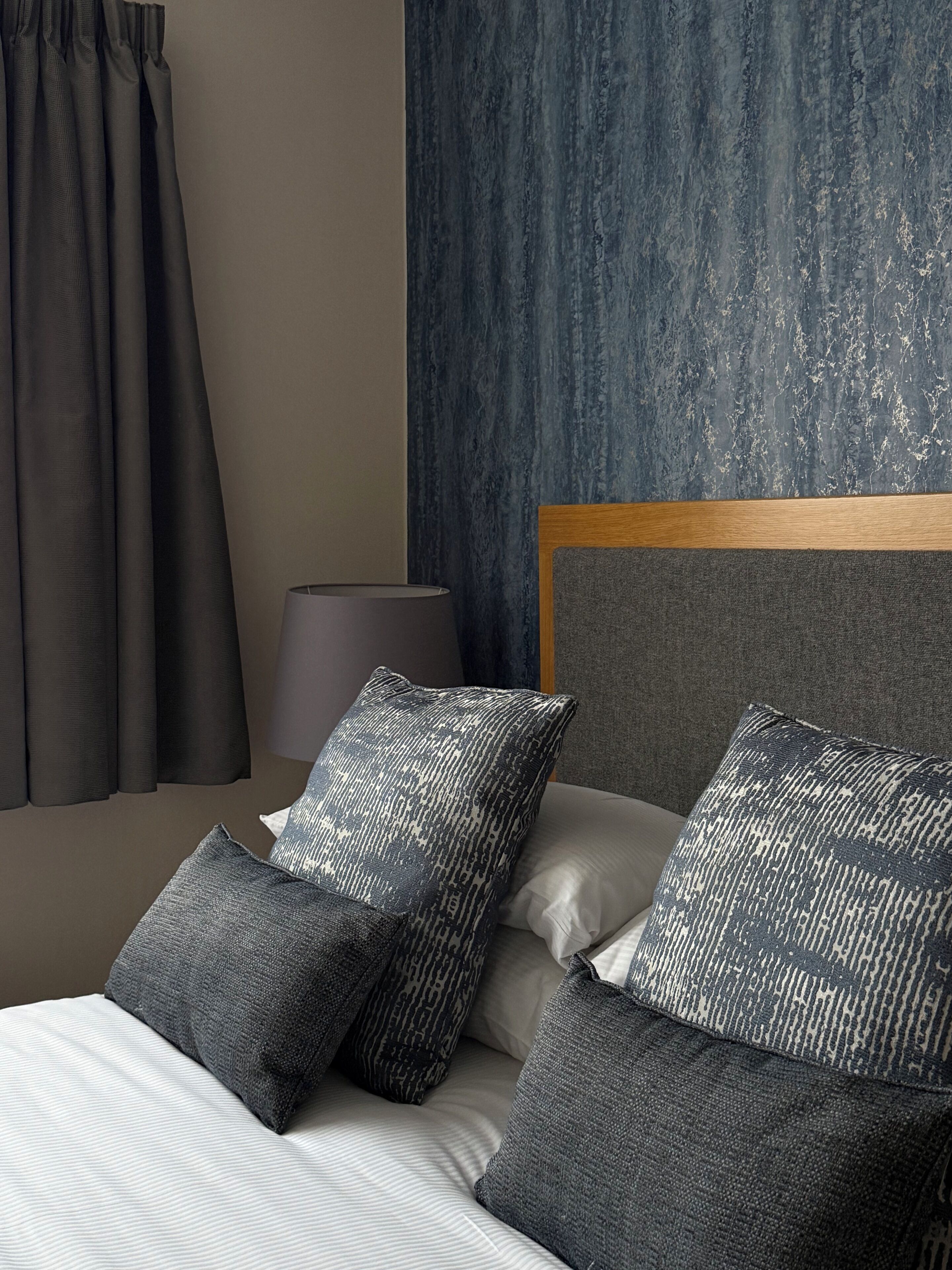 A neatly made bed with grey and white bedding, a wooden headboard, and grey patterned pillows.